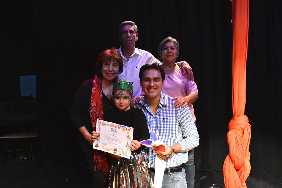 Familia posando en escenario, sostienen un diploma y un ramo, luego de concierto de kinder